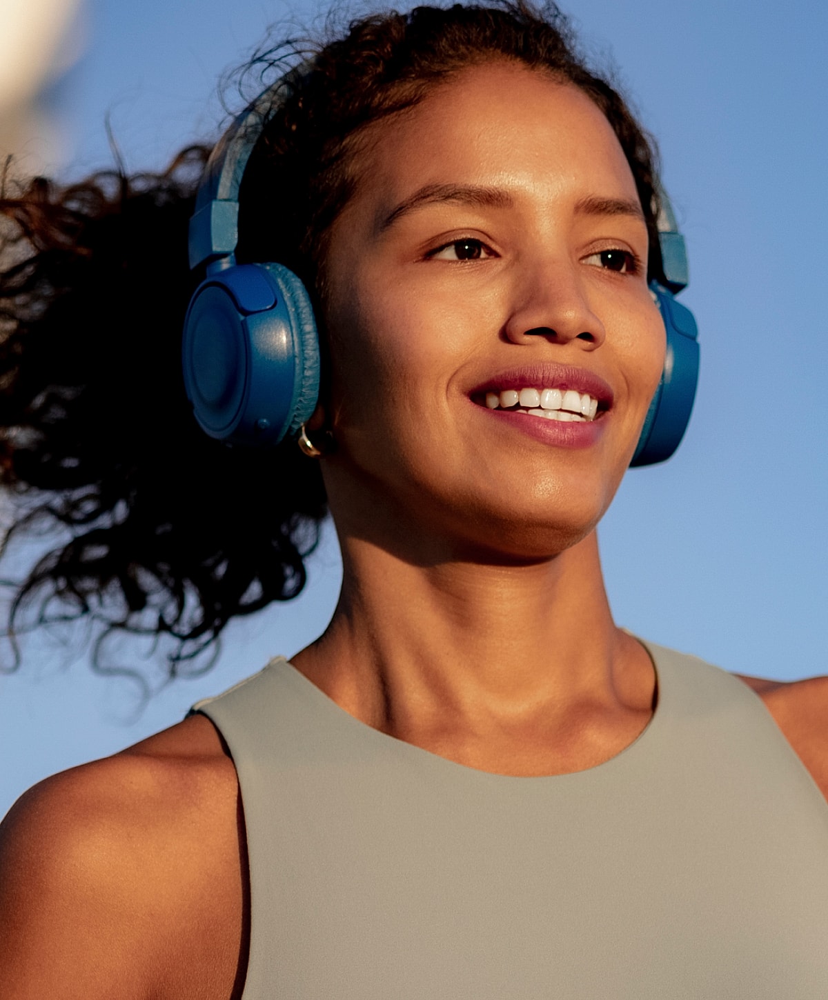Woman smiling with blue headphones outdoors.