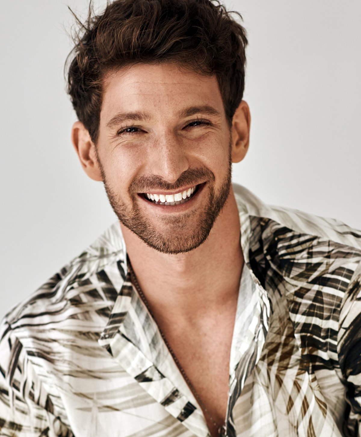 Smiling man in a patterned shirt, light background.