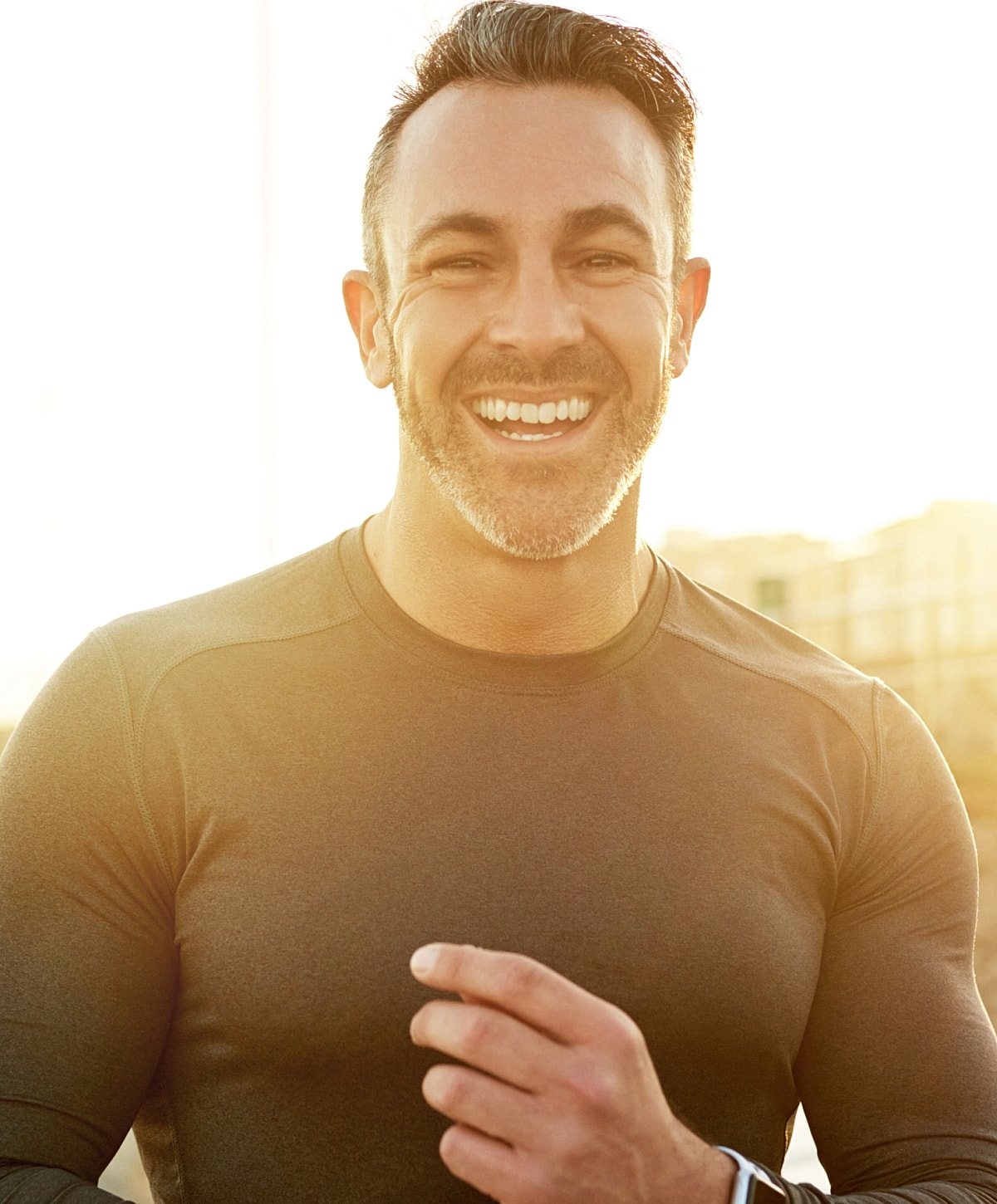 Smiling man in workout gear, sunlit background.