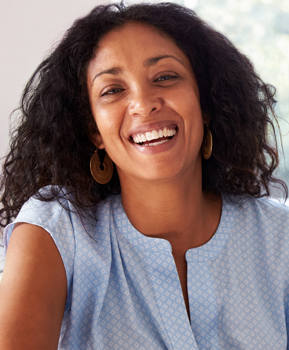 Smiling woman with curly hair in light clothing.