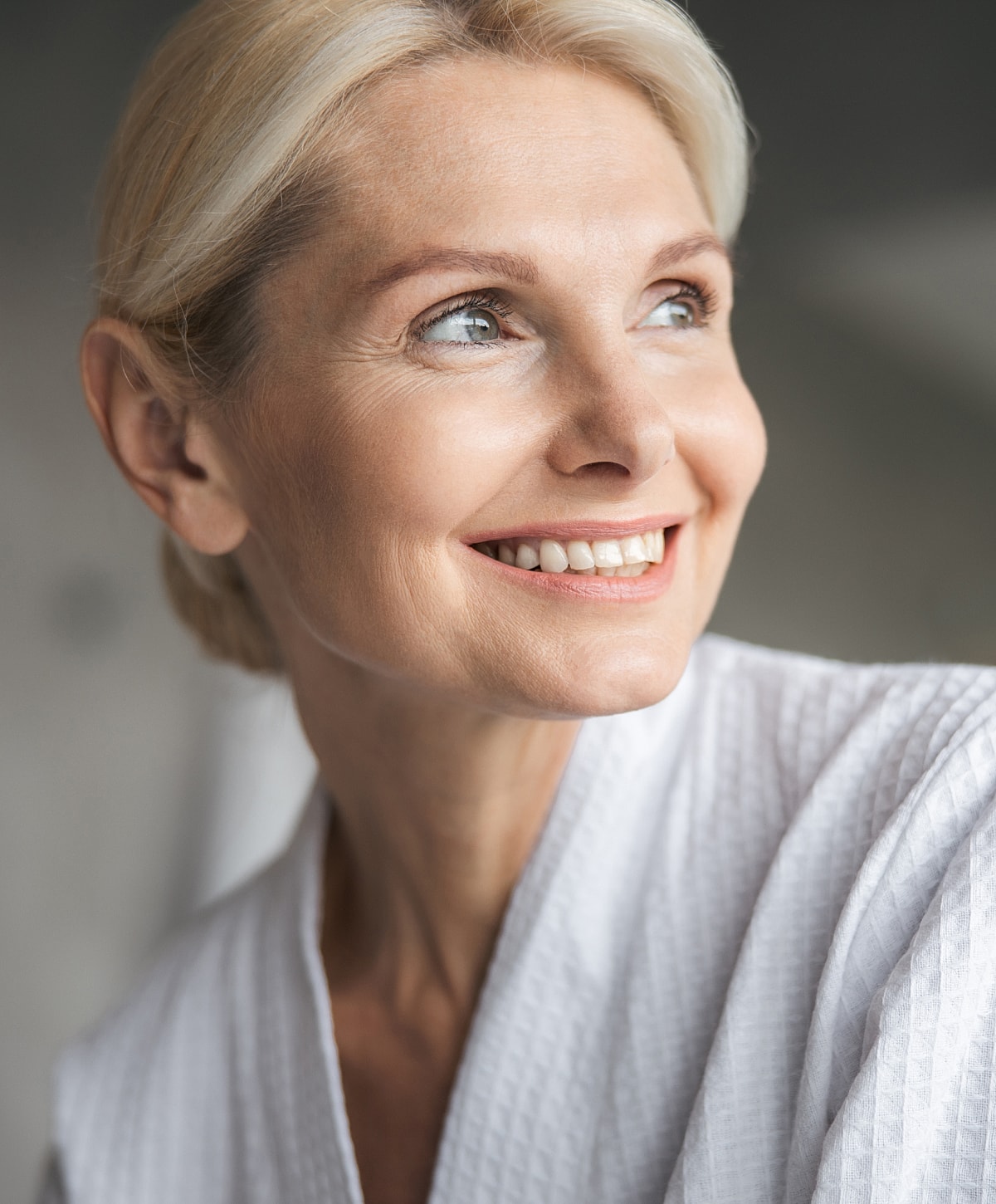 Smiling woman in a white robe, looking thoughtful.