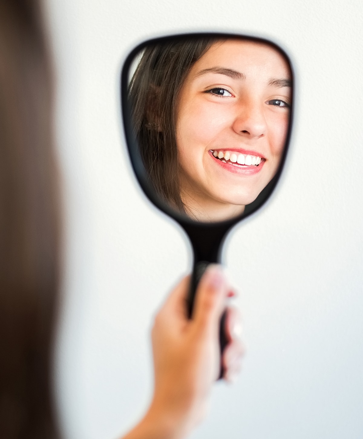 Smiling girl looking into a hand mirror.