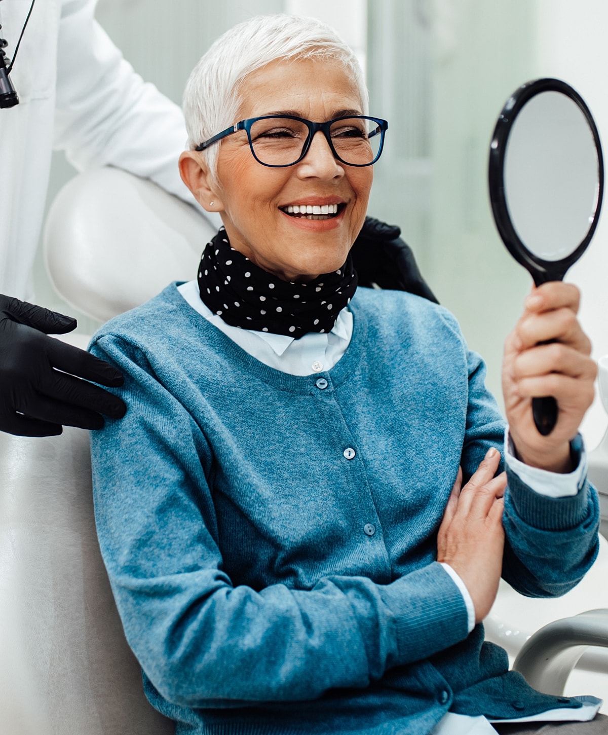 Smiling woman at dentist, holding mirror.