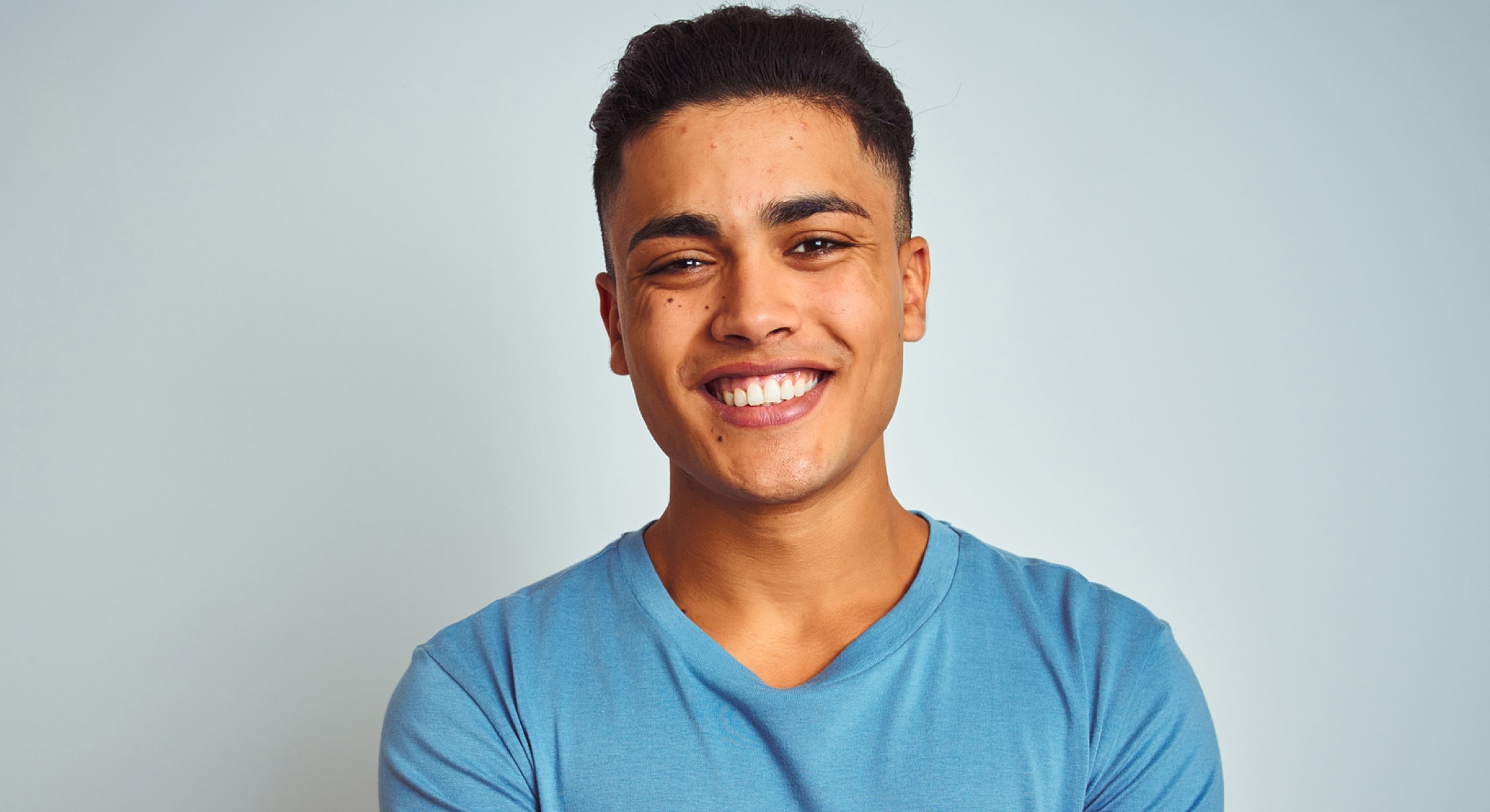 Smiling young man in blue shirt against backdrop.
