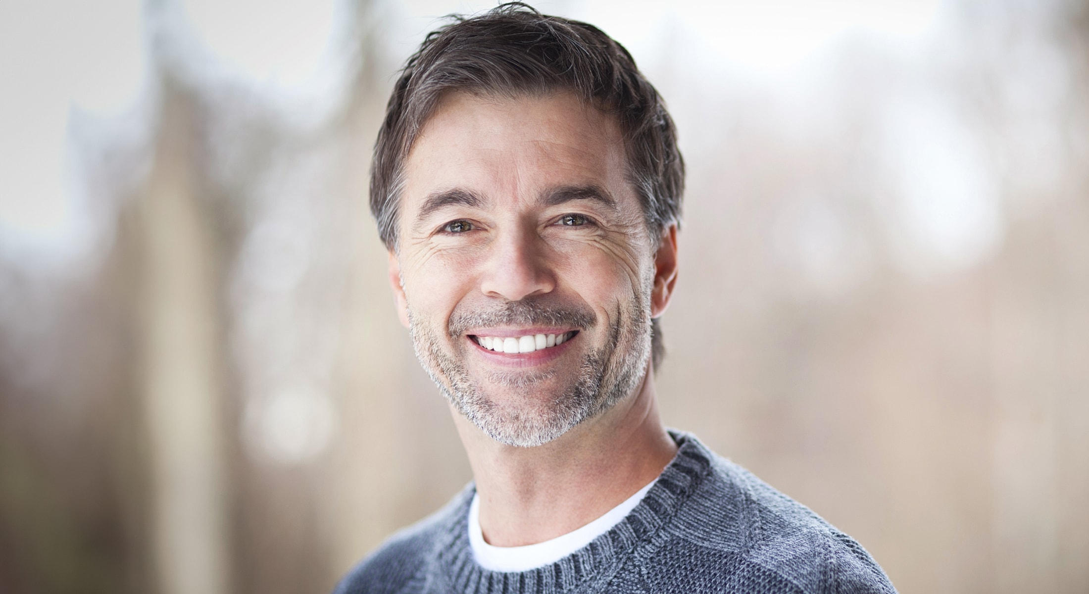 Smiling man in a cozy sweater outdoors.