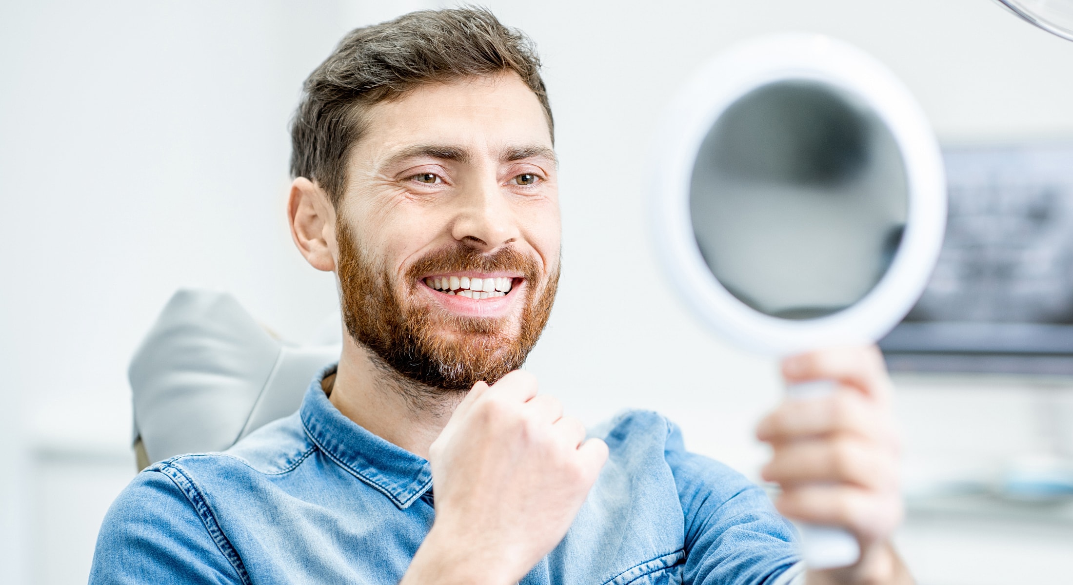 Smiling man examining teeth in handheld mirror